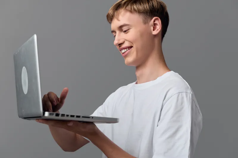 Smiling young male holding a laptop device, casual technology scene showcasing portable learning and modern gadget in hand, highlighting digital workflow and hands on interaction