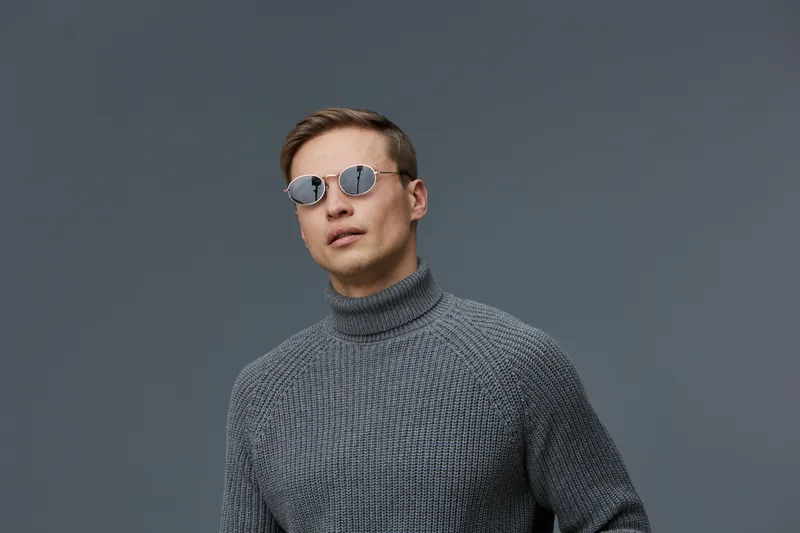 Man wearing stylish gray turtleneck sweater and fashionable round sunglasses look confident pose studio portrait isolated on neutral background contemporary fashion