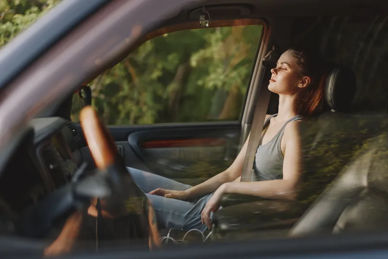 Young woman enjoying a moment of serenity in her car, basking in natural light with a calm expression, surrounded by greenery, ideal for relaxation concepts