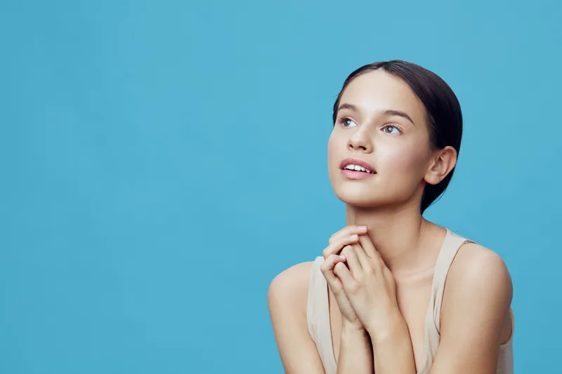 Young woman with a serene expression gazing upward against a blue background, showcasing beauty and tranquility, ideal for wellness and self care themes