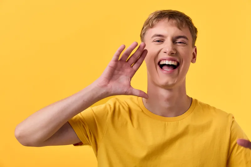 Cheering man shouting with hand near mouth against a vibrant yellow background, conveying excitement, voice projection, and bold expression suitable for marketing, promotion, and energetic campaigns.