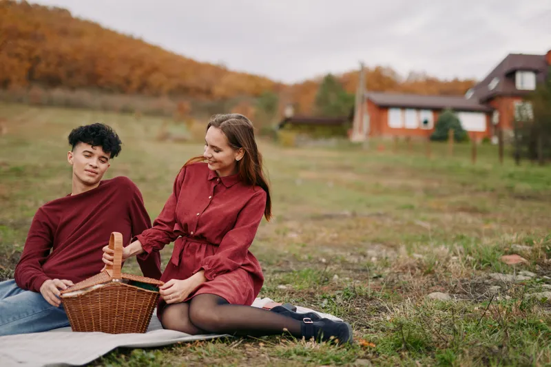 A candid outdoor picnic portrait of a young couple sharing a quiet moment on a blanket, conveying natural emotions, authenticity and veracity in everyday rural leisure and personal connection.