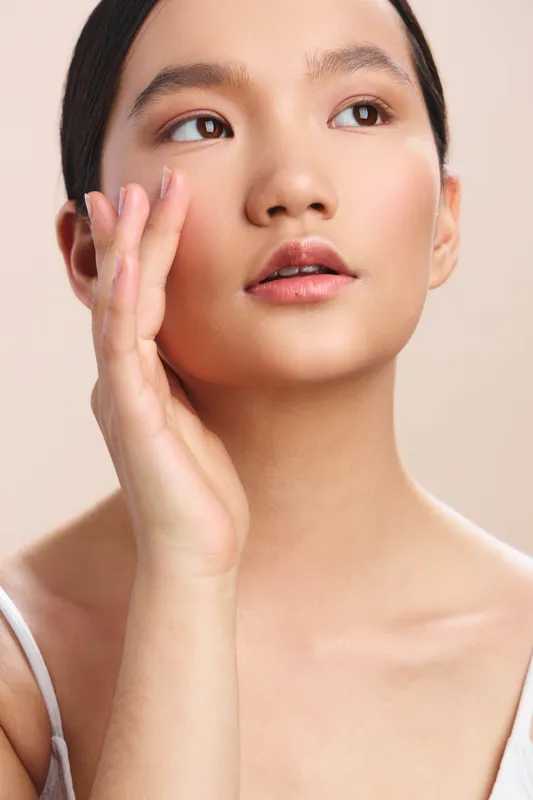 asian woman with clear skin gazes softly to the side, showcasing natural beauty, calm poise, gentle lighting, and a minimalist studio environment that conveys serenity and refined elegance.
