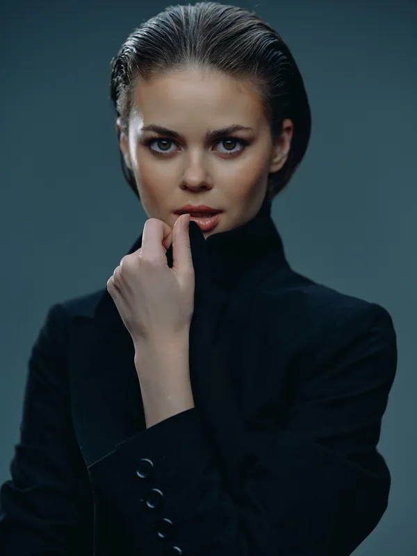 serious woman with short wet hair wearing black turtleneck posing with hand near face