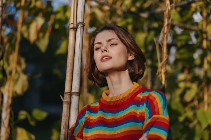 woman portrait sweater colorful outdoor nature, young female model in striped knitwear among green vines, short hair and soft sunlight, stylish autumn fashion headshot
