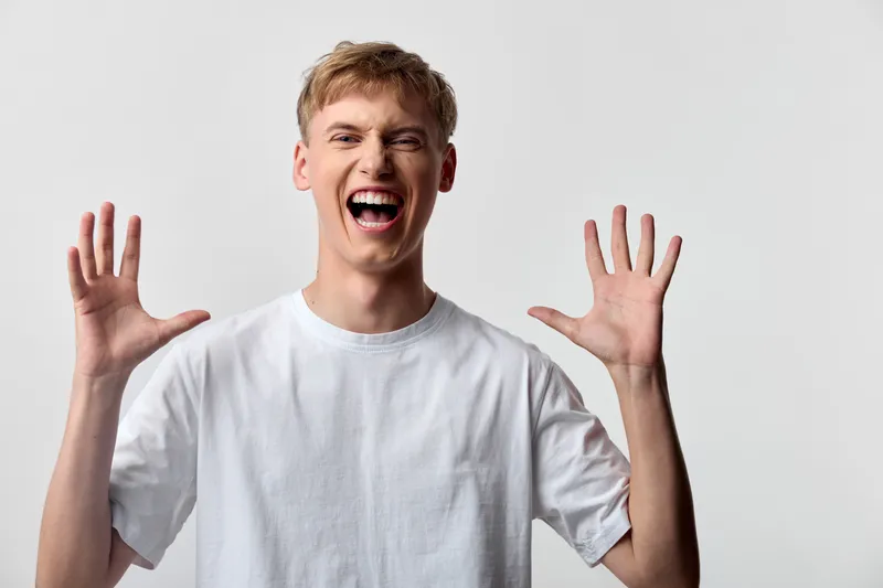 Smiling man with hands raised, front view in a bright studio, wearing a white shirt, conveying energy, enthusiasm, and a friendly vibe for lifestyle and promotion