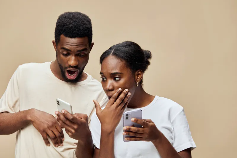 Surprised couple reacting to unexpected news on their smartphones, with neutral background and vibrant expressions, showcasing emotions of curiosity and excitement