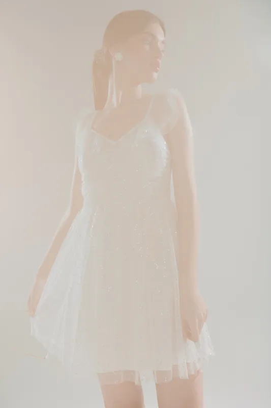 Young woman in a white lace dress poses gracefully against a soft background. The image highlights beauty, fashion, and elegance in a delicate, airy style.
