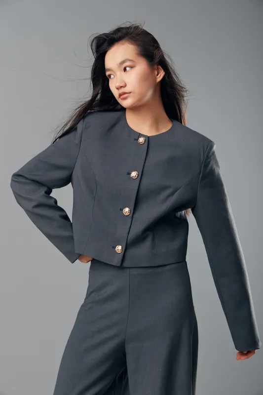 Young woman posing in a dark gray modern pantsuit with decorative buttons studio portrait isolated on gray background. Fashionable female model with long black hair and neutral expression.