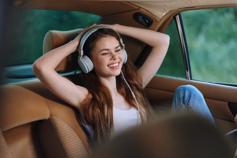 Young woman enjoying music in car, wearing headphones, smiling and relaxed, capturing the joy of commuting and a carefree lifestyle.