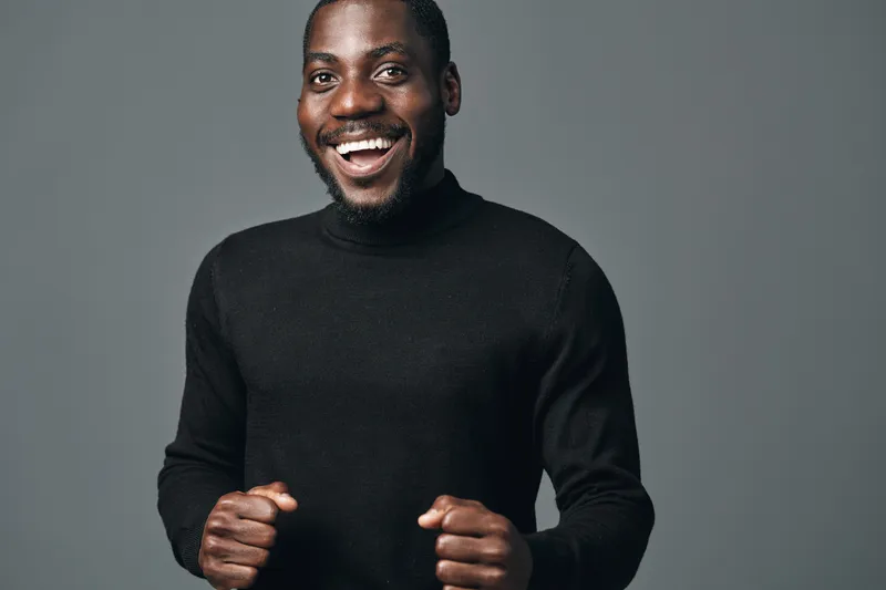 African man smiling and posing in black sweater with creative conceptual visual style on gray background. Happy male portrait with positive emotion and confident expression.