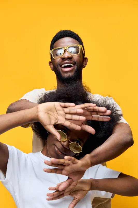 Happy young African couple celebrating together, wearing stylish eyewear against a vibrant yellow background, showcasing joy and connection