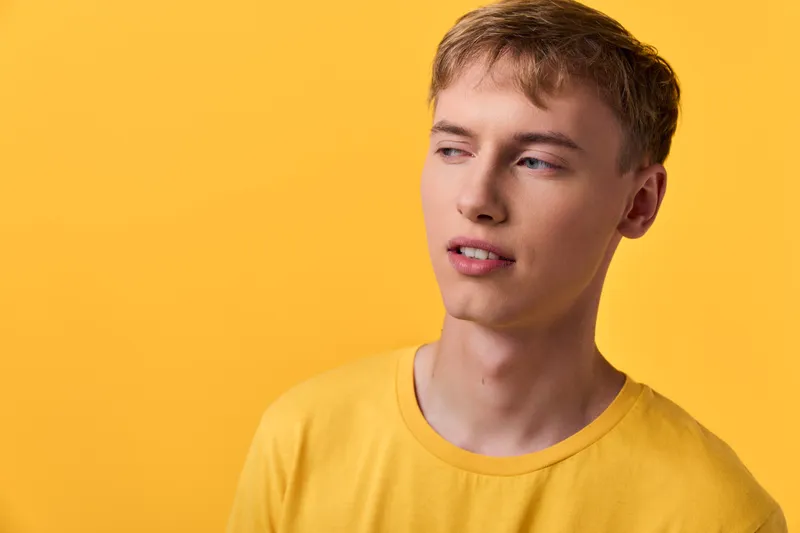 Man in a yellow shirt against a yellow backdrop, looking to the side with a thoughtful expression, studio setting, casual fashion and color harmony style