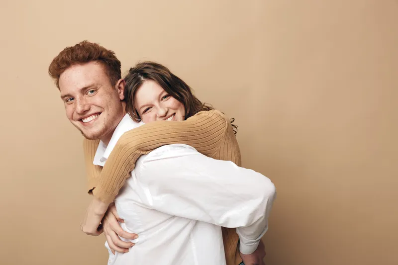 Happy young couple embraces and smiles in casual clothes against beige background. Concept of love, friendship, relationship, and joyful moments together in studio portrait.