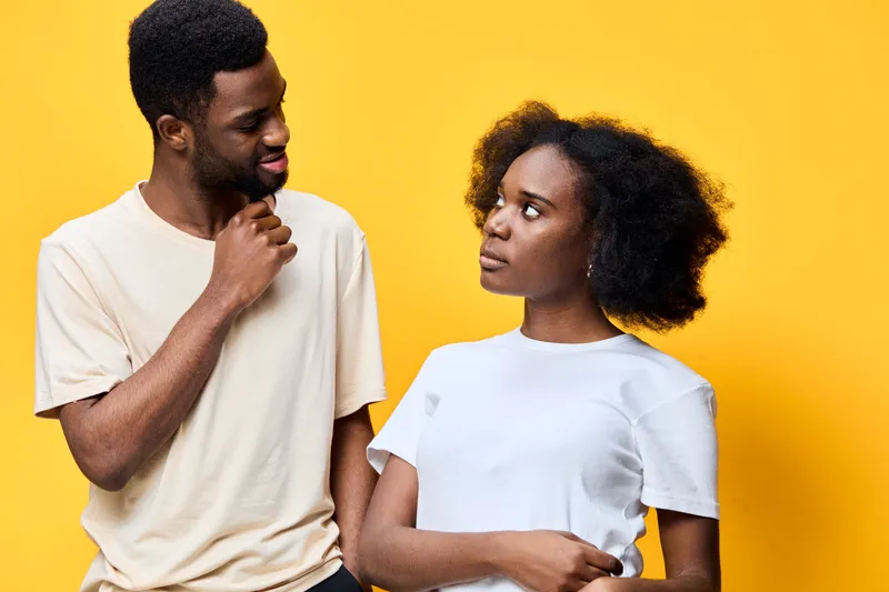 A cheerful young African couple engaging in a playful conversation, showcasing positive emotions against a vibrant yellow background