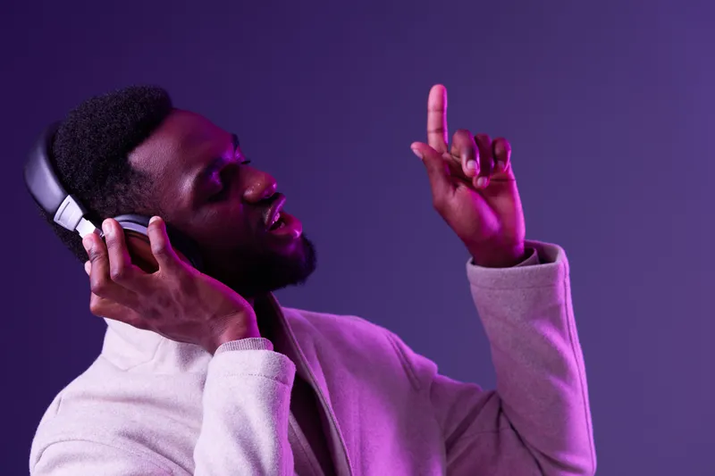 Young Black man enjoying music with headphones, expressing joy and energy against a vibrant purple background Perfect for music related themes