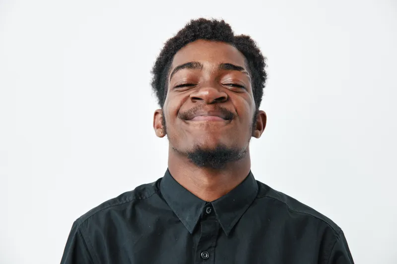 Young African American man with dark skin and short hair smiling with closed eyes wearing black shirt on white background. Portrait, happiness and confidence concept.