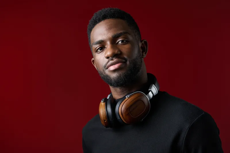 Stylish young Black man with headphones against a dark red background, conveying confidence and modernity Perfect for music related themes and lifestyle concepts