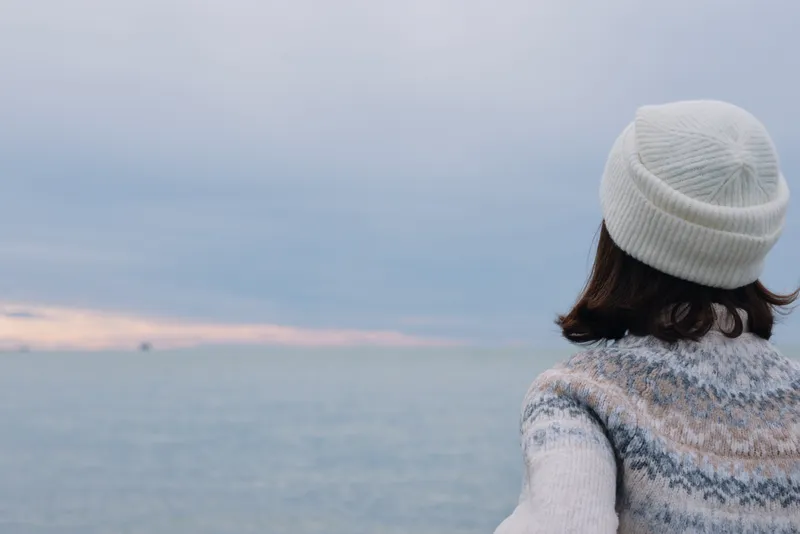 Sea, ocean, person, back, winter, sweater, beanie, shore, horizon, calm mood with distant waves and soft light as someone gazes at the sea in quiet reflection