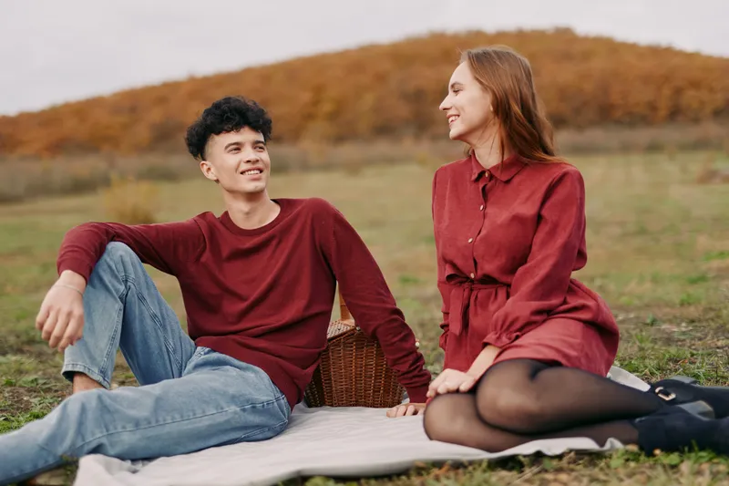 Candid outdoor portrait of a young couple sharing a genuine, authentic moment on a picnic blanket in an autumn field, conveying natural connection and quiet trust.