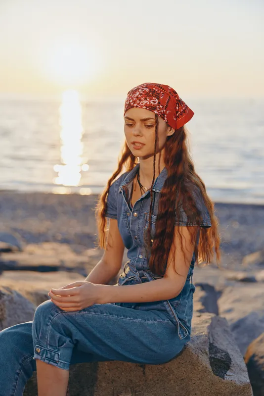 lifestyle woman in modern boho-western denim street style sitting by the sea during golden hour with film color warmth and relaxed expression