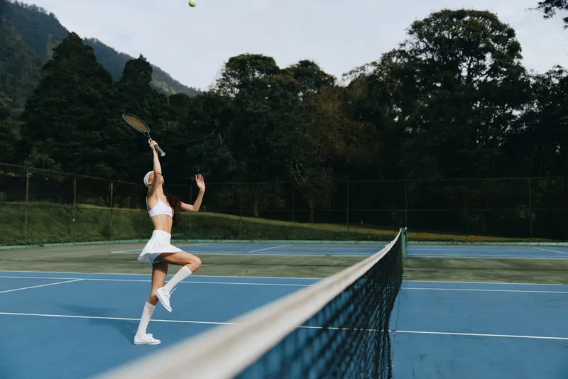 Energetic female tennis player in a white skirt and top, capturing the joy of summer sports with a bright green background and a clear blue sky