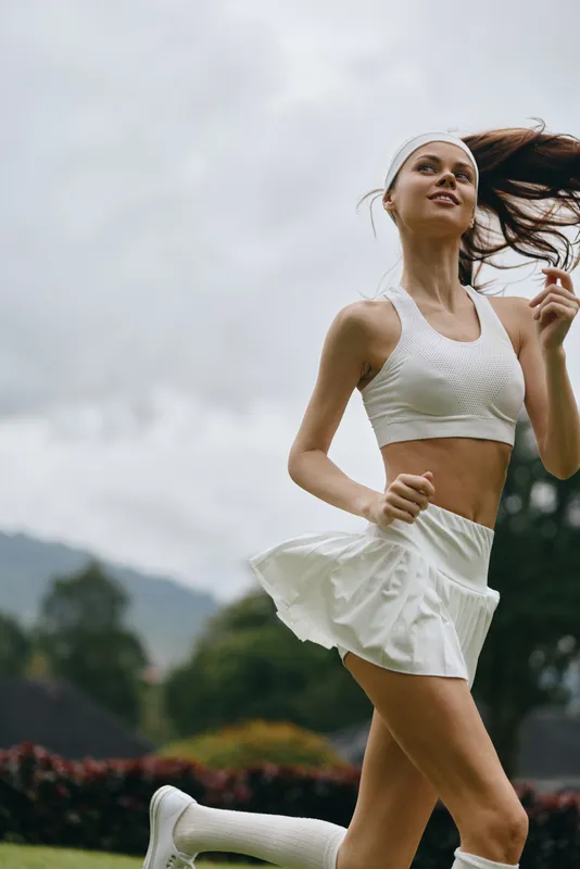 Young athletic woman running outdoors in a white sports outfit, showcasing a sense of freedom and vitality amidst a natural background
