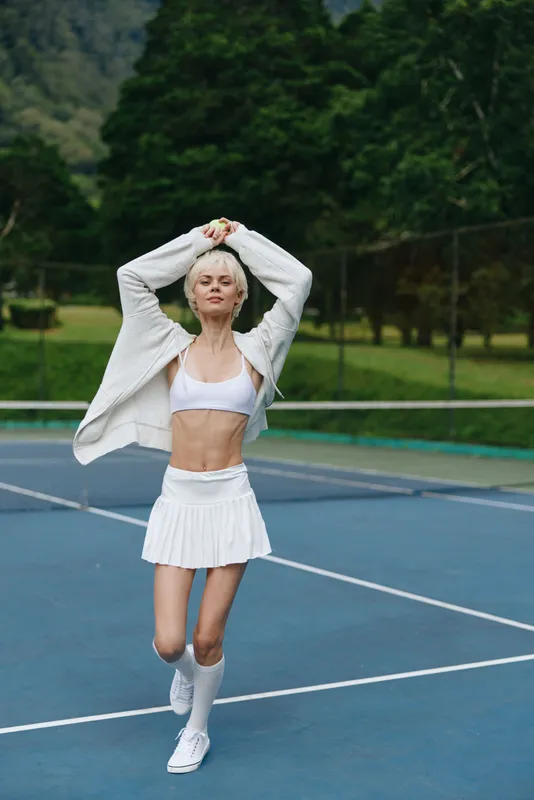 Cheerful athletic woman in a white outfit practicing tennis on a sunny day, showcasing an energetic spirit and commitment to fitness
