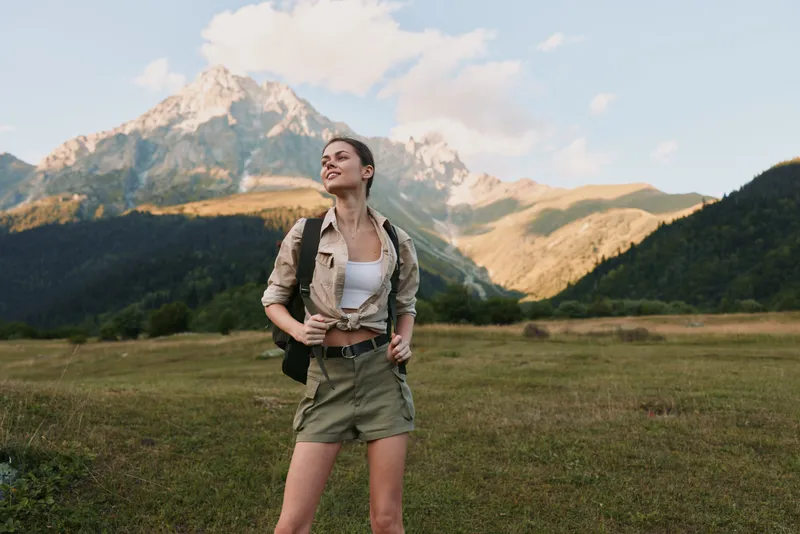 Woman hiker enjoying outdoor adventure in a mountainous landscape, wearing casual outfit with backpack, smiling as she explores expansive scenic valley