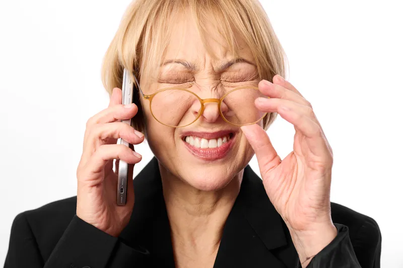 Smiling elderly business woman, wearing glasses, answers smartphone call, touching eyeglass frame, upbeat expression, close up portrait, isolated on white background