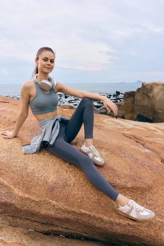 Fit young woman enjoying outdoor fitness in stylish activewear on rocky beach, showing confidence and relaxation amidst a natural landscape