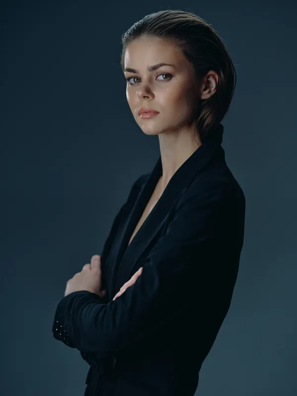 serious woman in black business suit with crossed arms posing confidently against dark background