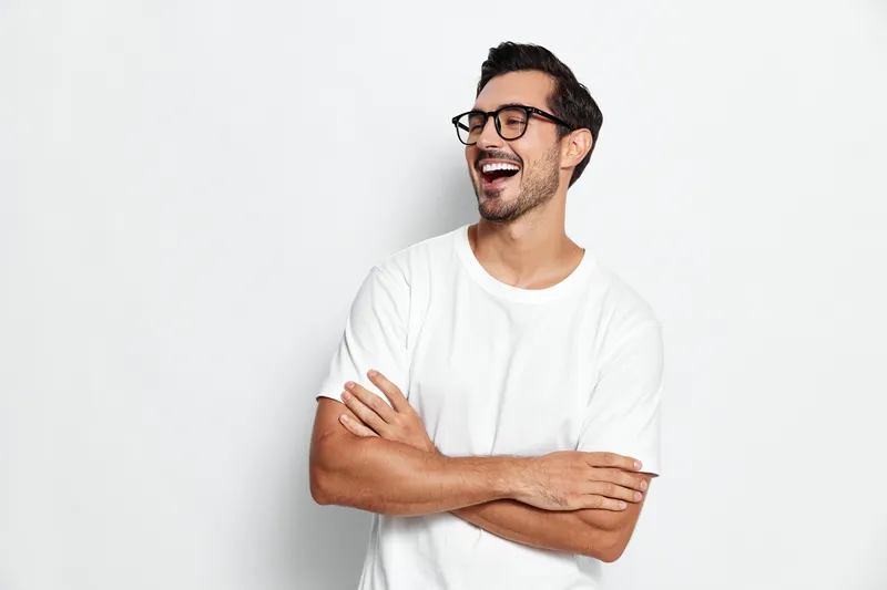 Full body smiling happy cheerful young man wear white t-shirt pose with arms crossed look away isolated on plain solid light background. People lifestyle concept