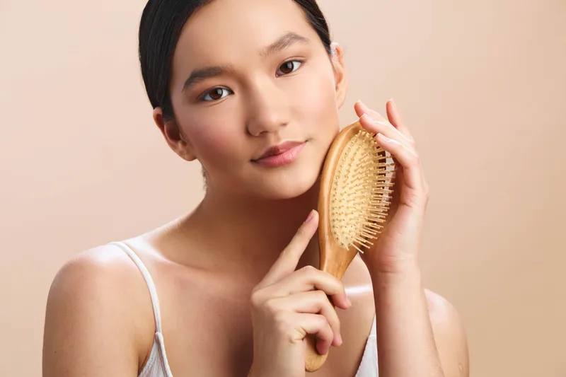 Asian woman brushing her hair in a softly lit studio, presenting a calm and elegant moment that highlights selfcare and natural beauty.