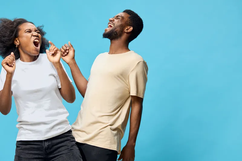 Joyful African couple celebrating with laughter, wearing casual clothing against a vibrant blue background, embodying happiness and connection, perfect for lifestyle themes