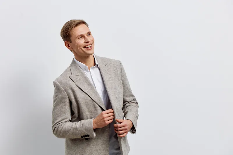 Smiling man wearing light grey blazer and white shirt pose against plain light grey background, cheerful expression, business casual style, studio portrait, positive mood, people lifestyle concept