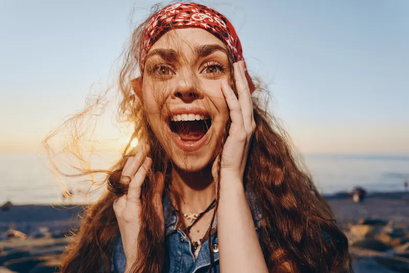 Lifestyle woman with modern boho-western denim street style, smiling joyfully with natural red hair and colorful headband in warm film color sunlight.