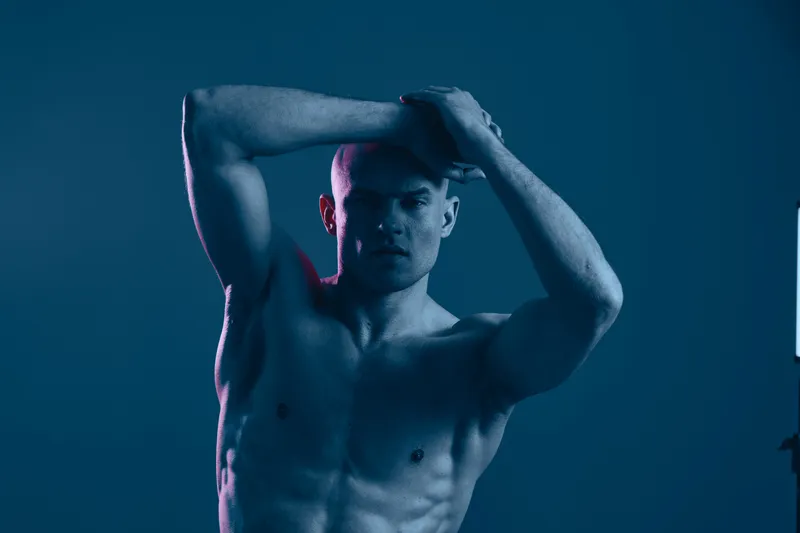Strong man posing in dramatic blue light, showcasing defined muscles and intense expression, creating a powerful and captivating visual impact.