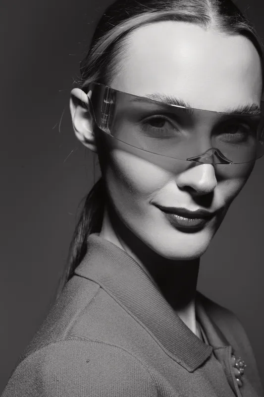 Portrait of a young white woman with fair skin wearing futuristic transparent glasses and a stylish jacket in a dramatic black and white studio setting. Concept of fashion and modern style.