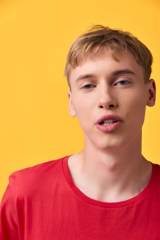 Close up of a young man in a red shirt against a bright yellow background, capturing a casual expression and modern fashion vibe ideal for lifestyle, social media, and advertising visuals