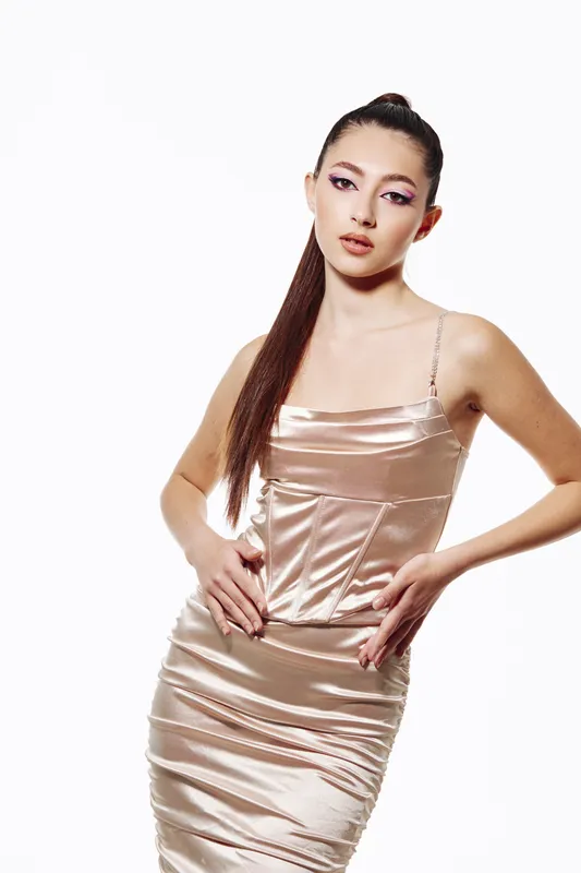 Elegant young woman with long straight hair wears shiny satin dress posing on white background. Makeup with colorful eyeshadow enhancing beauty and fashion concept. Creative beauty studio shot.