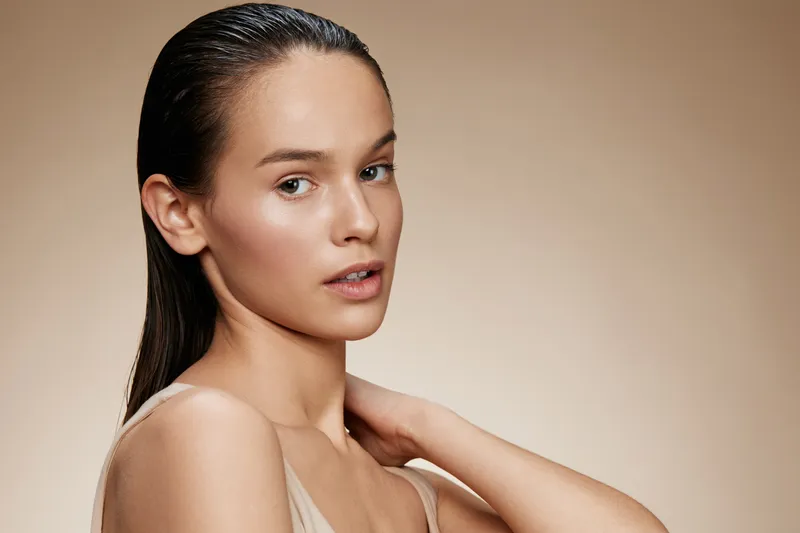Elegant portrait of a young woman with wet hair, showcasing natural beauty and soft skin tones against a neutral background Emphasizes confidence and sophistication