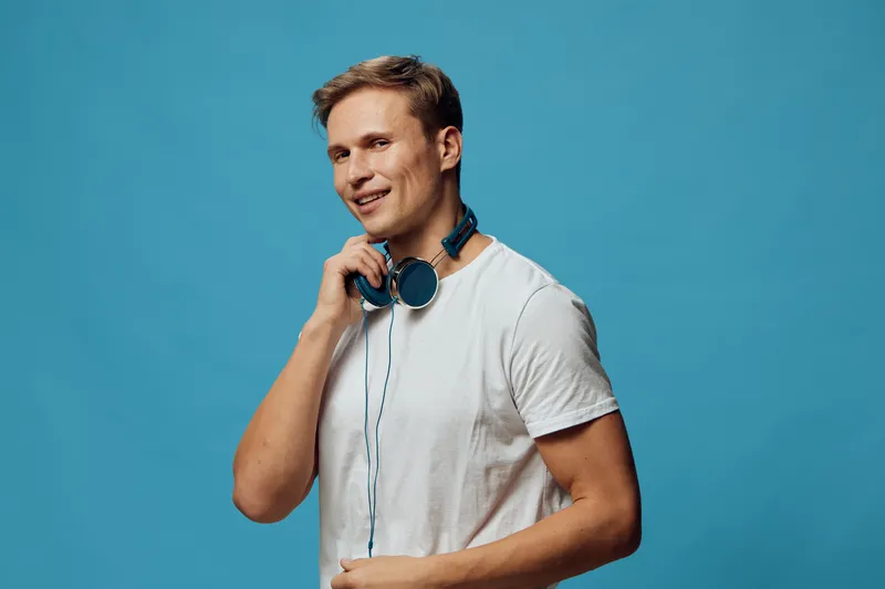 Smiling man with headphones casual clothing isolated on blue background studio portrait. Music lifestyle concept