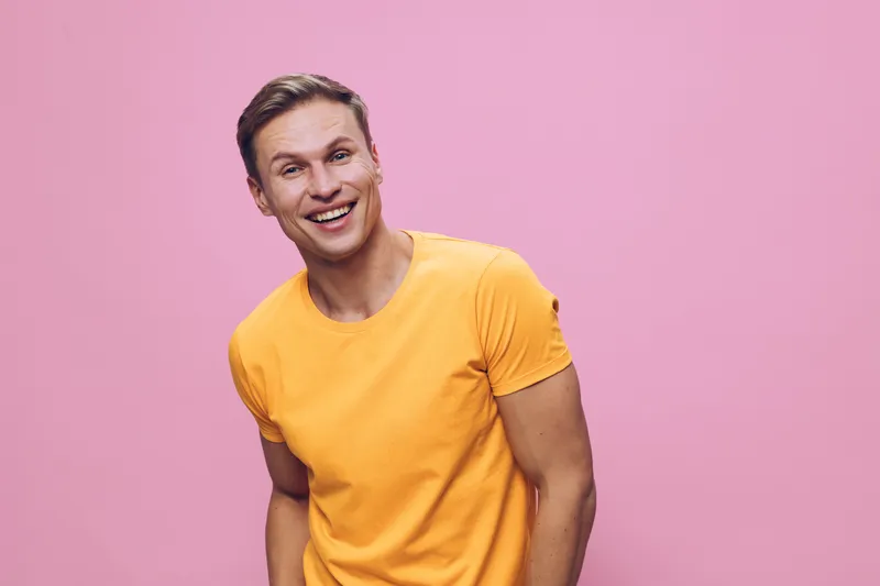 Happy smiling young caucasian man wearing yellow t-shirt looking at camera posing on pink background digital nomad remote work concept