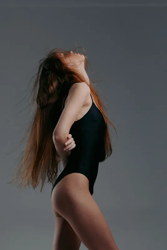 graceful woman in black bodysuit with long hair posing against gray background
