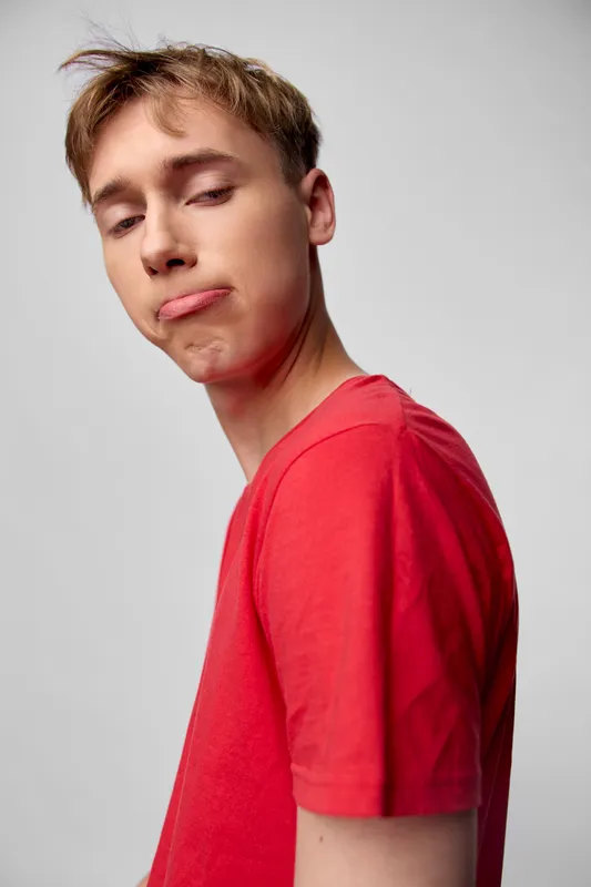 Young man with a silly face in a red shirt, casual style and playful mood, expressive pose for lifestyle or fashion stock imagery for marketing use online.