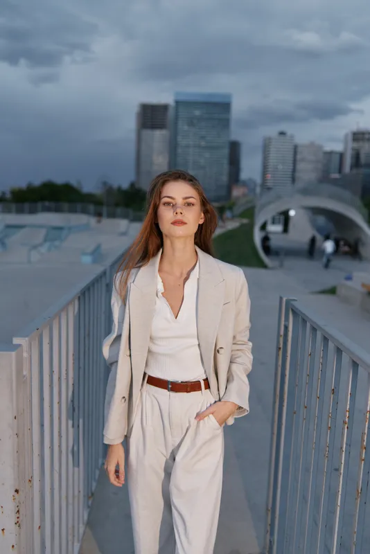 Confident woman in beige business casual outfit walking in urban environment with skyscrapers and modern architecture in overcast weather KEYWORDS confident woman, business casual, urban environment, 