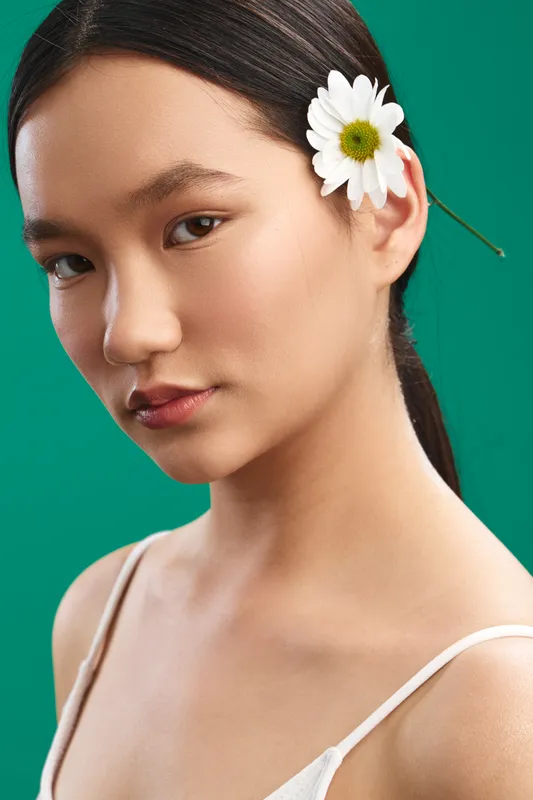 asian woman portrait in close up, flower tucked behind ear, calm expression, soft studio lighting, minimal background, elegant and serene mood and atmosphere.