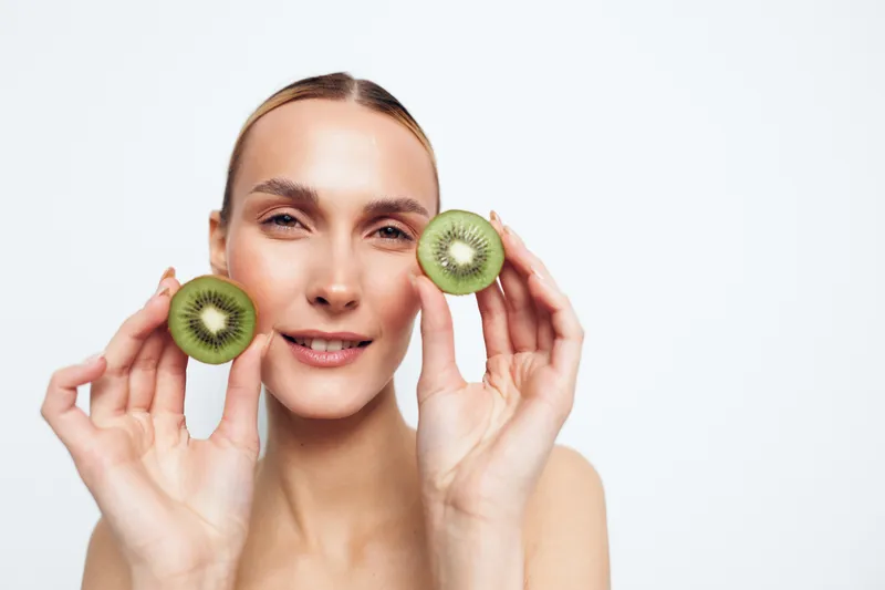 Woman holding kiwi slices for skincare, close up portrait, fresh beauty and wellness, self care concept, fruit on white background, soft studio lighting, healthy skin