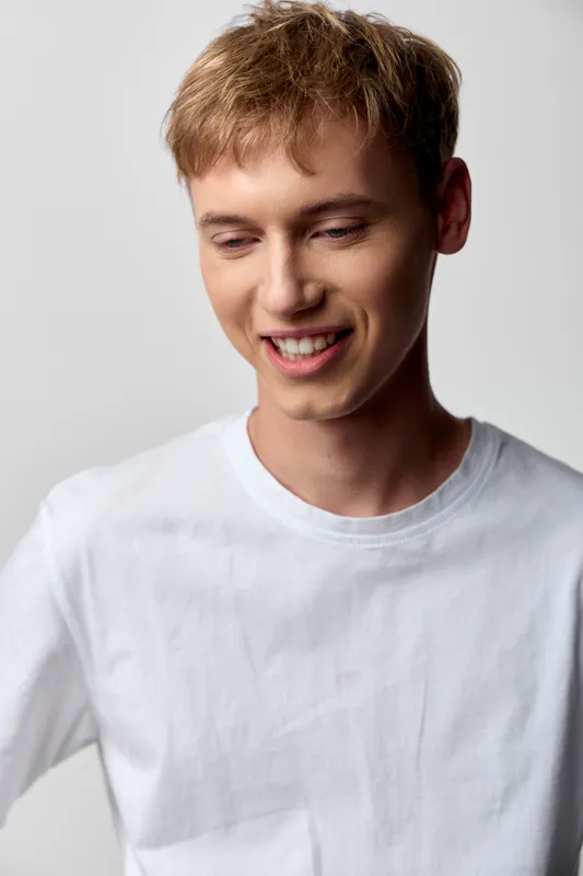 Smiling man in white shirt in a studio setting for casual lifestyle imagery, natural light and relaxed mood, focused on friendly and approachable look in a clean background